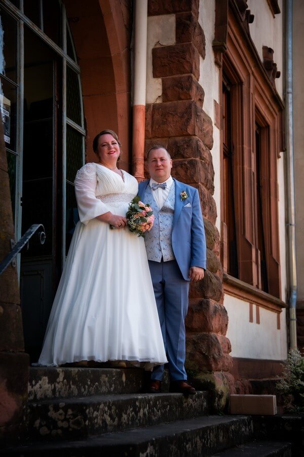 Curvy Braut in fließendem Chiffonkleid mit Puffärmeln und Dekolleté, Bräutigam in Wilvorst-Anzug in Blau mit Weste und Fliege – Plus-Size Hochzeit bei Biancas Brautmoden