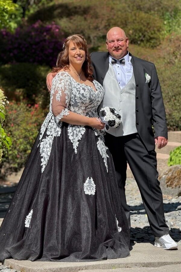 Curvy Braut im maßgeschneiderten schwarz-weißen Brautkleid (Gr. 58) und Bräutigam in Tziacco-Anzug mit Stehkragen, grauer Weste und Holzfliege – Hochzeit in großen Größen