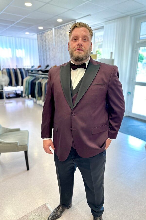 Bräutigam in Übergröße trägt bordeauxroten Smoking mit schwarzem Revers – festliche Herrenmode bis 7XL bei Biancas Brautmoden