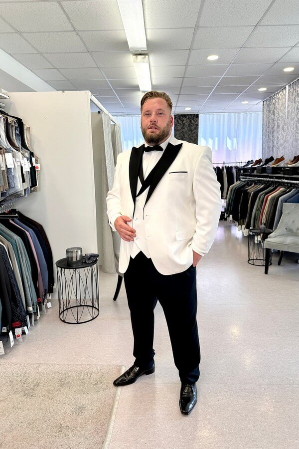 Bräutigam in großer Größe trägt hellbeigen Smoking mit schwarzem Revers, schwarzer Hose und zweifarbiger Weste – festliche Hochzeitsmode bei Biancas Brautmoden