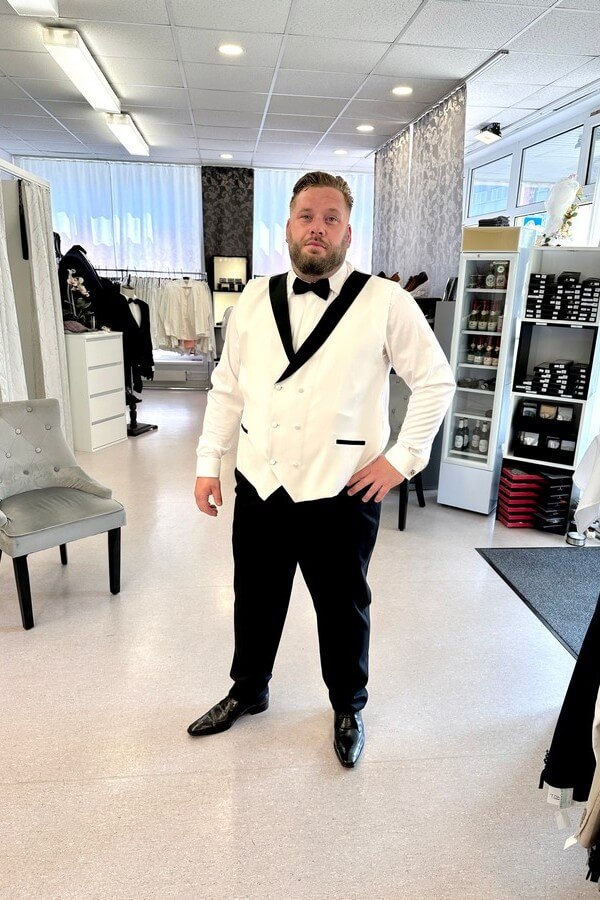 Bräutigam in großer Größe trägt hellbeigen Smoking mit schwarzem Revers, schwarzer Hose und zweifarbiger Weste – festliche Hochzeitsmode bei Biancas Brautmoden