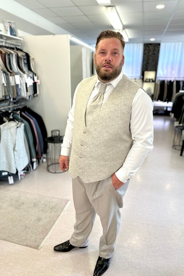Bräutigam in großer Größe trägt eleganten Tziacco-Gehrock mit Stehkragen, gemusterter Jacke und Plastron – Hochzeitsanzug in Beige bei Biancas Brautmoden