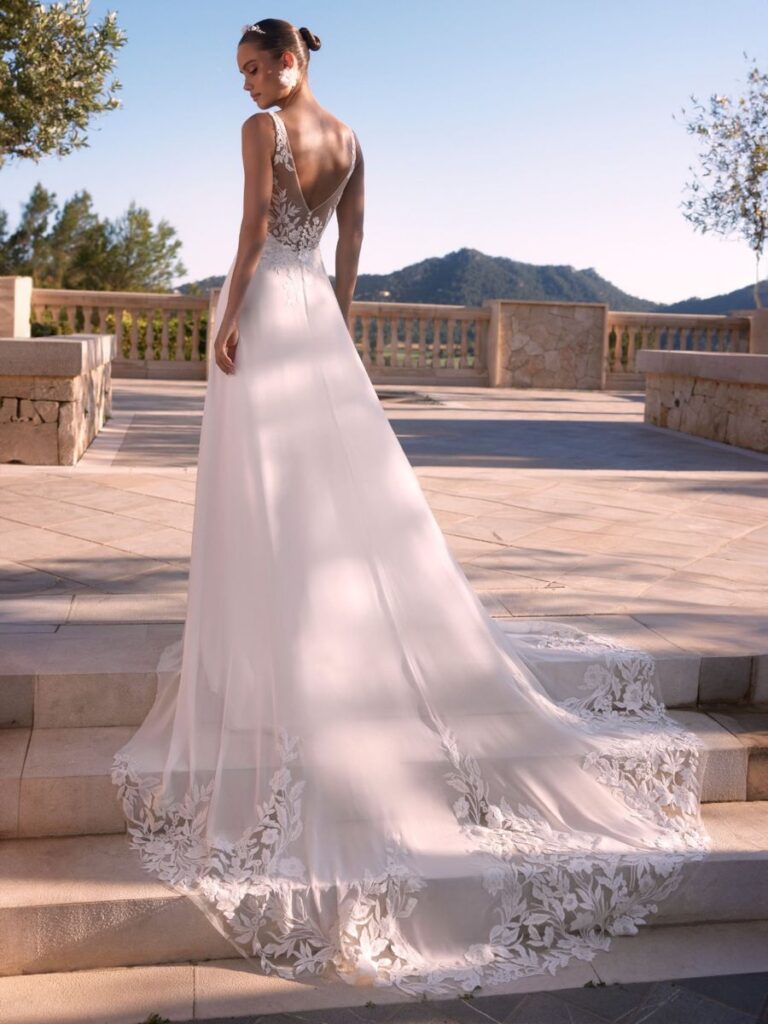 Besonderes Brautkleid Ione mit eleganter Schleppe, die von einem breiten Spitzenrand eingerahmt ist.