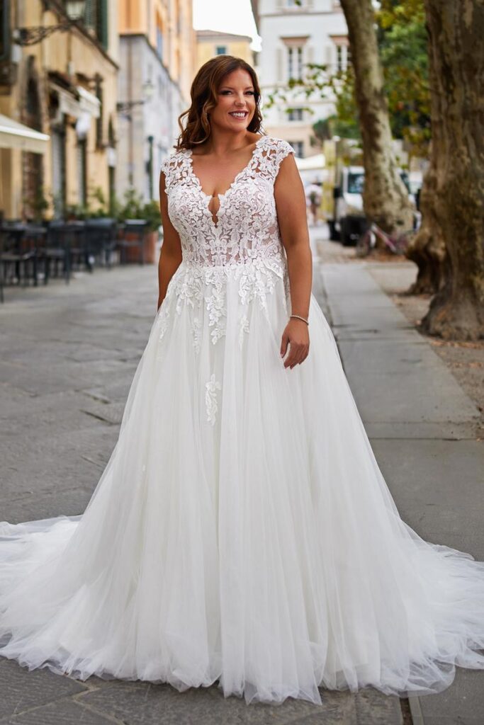 Curvy Brautkleid 2026 mit transparenter Spitzen-Corsage, tiefem Ausschnitt und weitem Tüllrock von Bianca’s Brautmoden