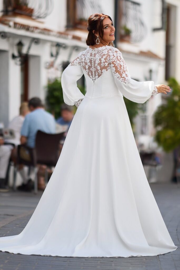 Curvy Brautkleid 2026 mit transparenter Spitzenrückenpartie, langen Chiffonärmeln und fließender Schleppe von Bianca’s Brautmoden